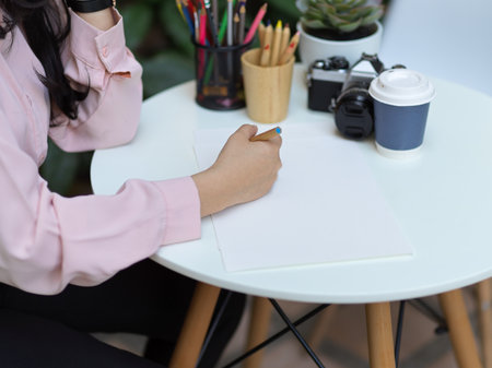 Cropped shot of female student hand drawing on mock up paper on coffee table in cafeの写真素材