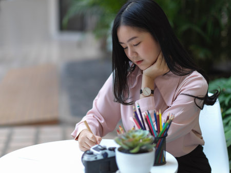 Portrait of female student concentrating on her drawing on coffee table in cafeの写真素材