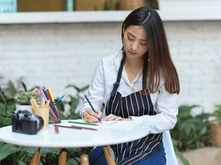 Portrait of of female artist with apron painting with coloured pencil on coffee table in garden