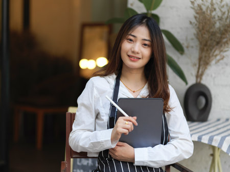 Portrait of waitress smiling to camera and holding digital tablet ready to take order in restaurantの写真素材