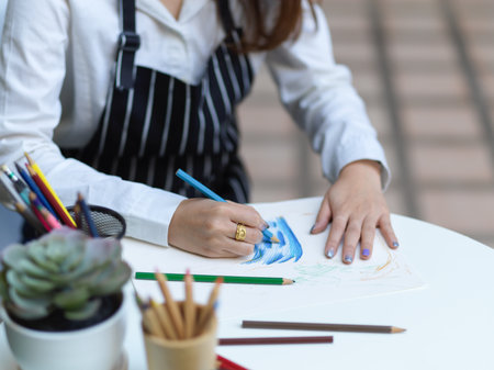 Cropped shot of female artist with apron painting on coffee table in gardenの写真素材