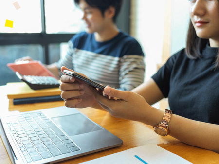Side view of female office workers using smartphone while working next to her colleague in meeting roomの写真素材