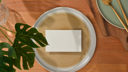 Top view of dining set with mock up name card on mock up ceramic plate and brass spoon and fork