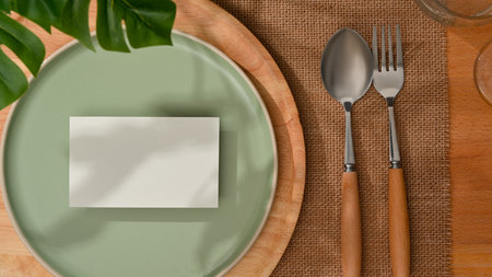 Top view of mock up card on mock up ceramic plate and silverware on wooden dining table