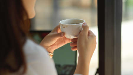 Close up view of female hands holding coffee cup while relaxing from work in cafeの写真素材