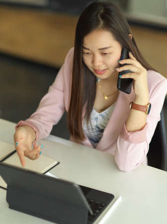 Top view of businesswoman talking on the phone while working with digital tablet on the tableの写真素材
