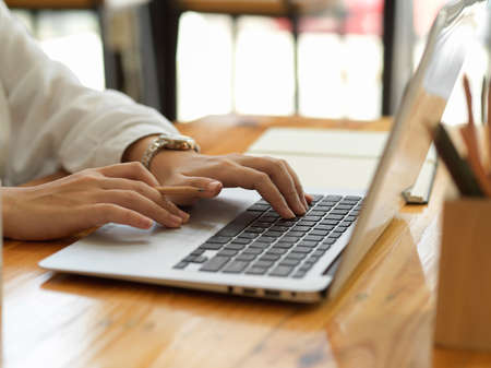Side view of female hands typing on laptop keyboard and working with stationery on wooden table