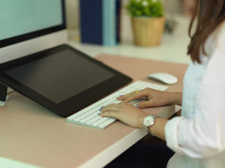 Side view of female office worker hand typing on computer keyboard on worktable in office roomの写真素材