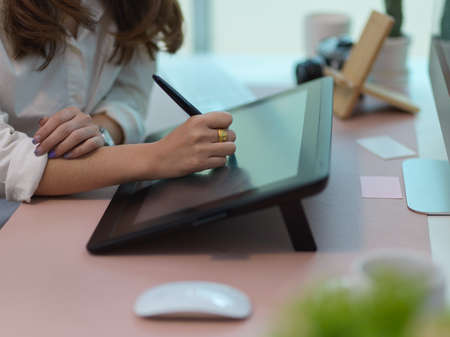 Side view of female working with drawing tablet and computer device in office roomの写真素材