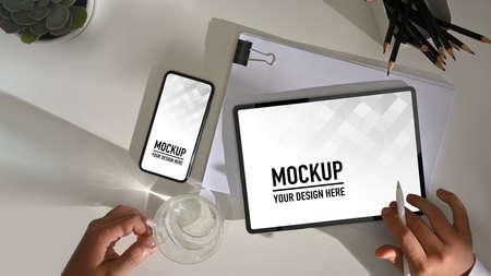 Top view of male hand working with digital tablet, smartphone and paperwork on white table