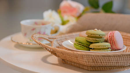Close up view of a plate of French colourful macarons on wicker tray and tea cup on coffee tableの写真素材