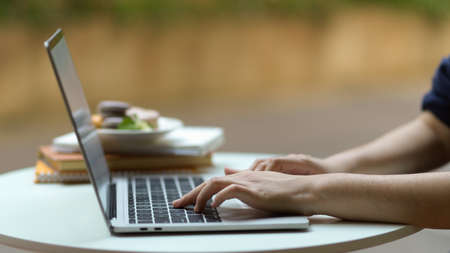 Side view of female hand typing on laptop keyboard on coffee table in garden at homeの写真素材