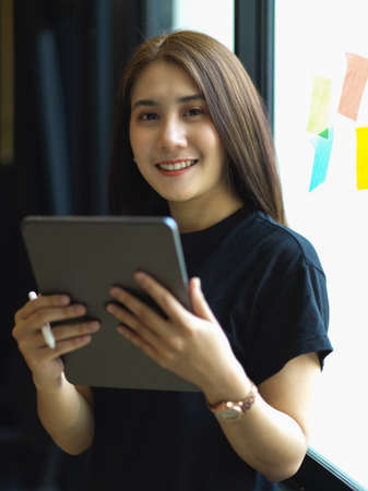 Portrait of female office worker smiling to camera while working with digital tablet in office room