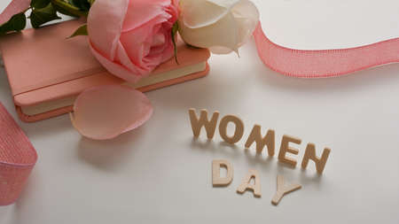Women's Day message with notebook, pink roses and ribbon decorated on white table backgroundの写真素材