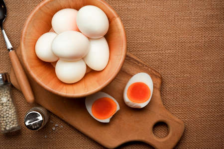 Top view of a lot of boiled eggs in wooden bowl and half sliced boiled egg on the kitchen tableの写真素材