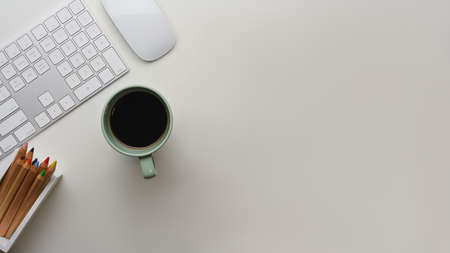 Creative flat lay of workspace with computer keyboard, mouse, coffee cup and coloured pencils on the tableの写真素材