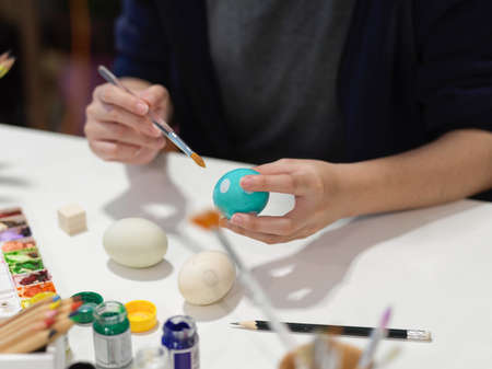 Close up view of female hands painting Easter eggs with poster colour and other paint tools