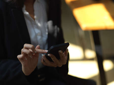 Close up view of businesswoman using smartphone while sitting on the chair in cafeteriaの写真素材