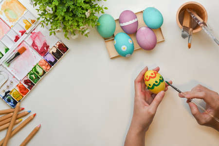 Top view of female hands painting on eggs to prepare for Easter festival on craft table with paint toolsの写真素材