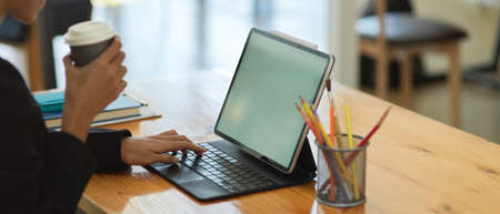 Side view of businesswoman holding paper cup to drink coffee while working with digital tablet