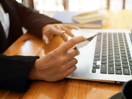 Side view of female holding credit card and typing on laptop keyboard to online paying