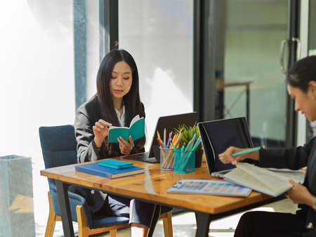 Cropped shot of two female office workers working together while sitting opposite each other in office roomの写真素材