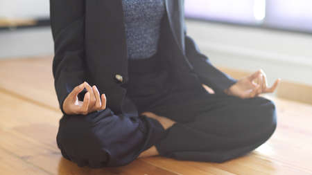Cropped shot of female worker sitting in yoga position and meditating on the table in meeting room
