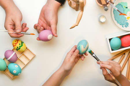 Top view of two people hands painting on eggs, preparing for Easter festival at home