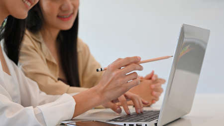 Side view of two young pretty female students doing assignment with laptop on the table in library