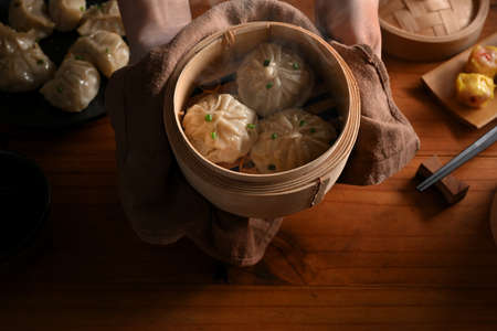 Top view of hands holding bamboo steamer with dumplings to show to camera above kitchen tableの写真素材