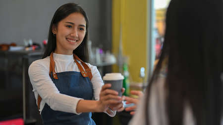 Portrait of young beautiful female giving a cup of beverage to her customer in coffee shop