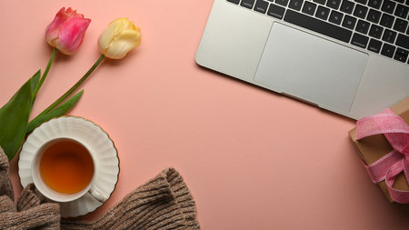 Top view of pink creative workspace with teacup, flowers, laptop and copy space in home office room