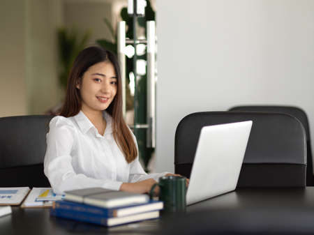 Portrait of businesswoman smiling to camera while working with laptop in office room