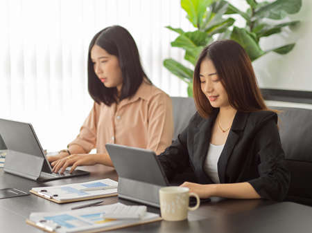 Portraits of two businesswomen sitting next touch other and working together in meeting roomの写真素材