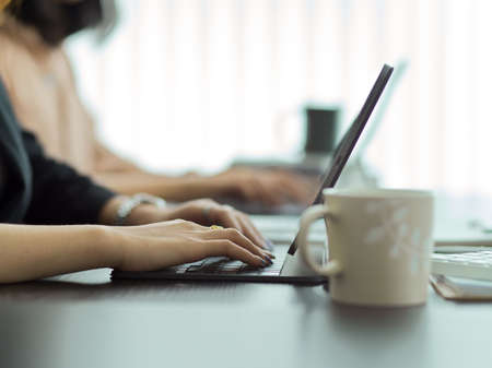 Side view of female hands working with digital tablet on meeting table with coffee mugの写真素材