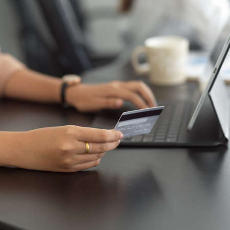 Close up view of female hand holding credit card and typing on tablet keyboard on the table in office roomの写真素材
