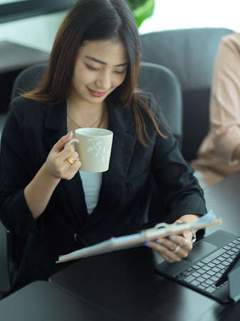 Portrait of businesswoman drinking coffee while reading business document in meeting roomの写真素材