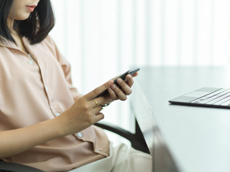 Side view of female office worker using smartphone while relaxing at workplaceの写真素材