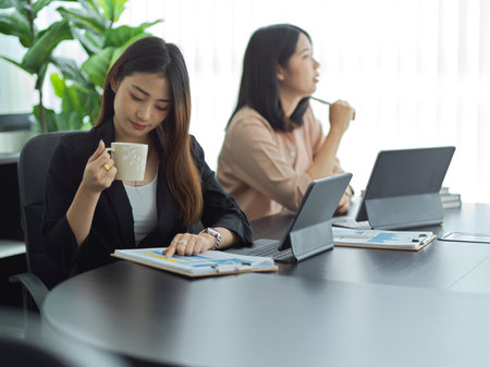 Portraits of two businesswoman working with digital tablet while sitting next to each other in meeting roomの写真素材