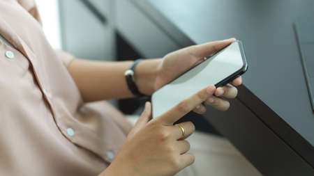 Cropped shot of female hands holding mock up smartphone while sitting at workplaceの写真素材