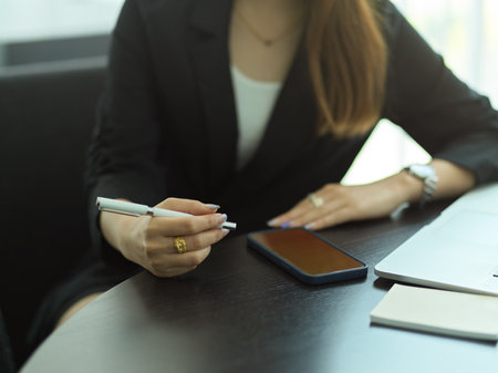 Cropped shot of businesswoman with pen in her hand working with smartphone and stationeryの写真素材