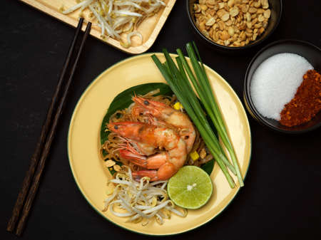 Top view of stir fired Thai noodles with shrimps serving on black plate with lime, beansprouts and chives, Pad Thai, black tableの写真素材