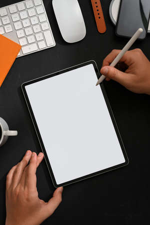 Top view of male hand using digital tablet on creative workspace with accessories and supplies,...