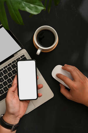 Top view of male working with smartphone and laptop on workspace with coffee cup and plant pot