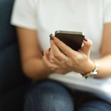 Cropped shot of female office worker using smartphone in her hands while relaxing in cafe