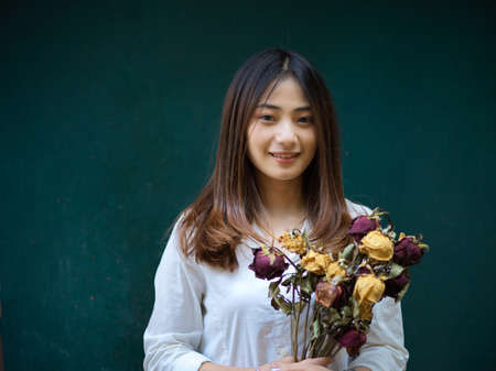 Portrait of young beautiful female holding flowers bunch and smiling to camera in dark green...