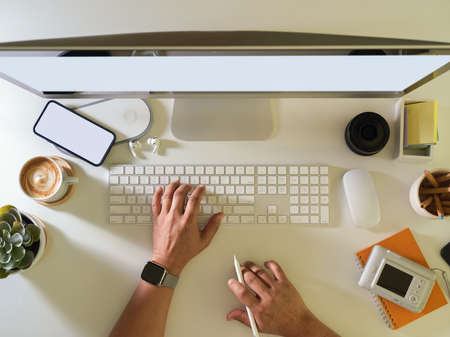 Overhead shot of male hand typing on computer keyboard on workspace with smartphone and supplies