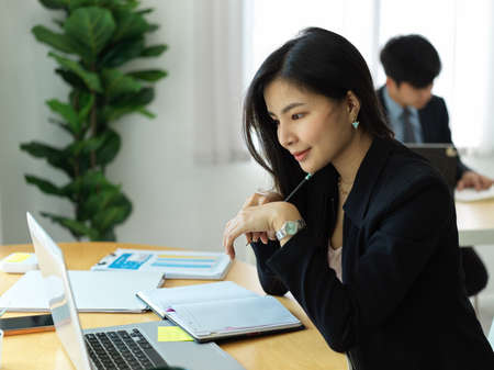 Side view of businesswoman concentrating with informations on laptop while working in office roomの写真素材