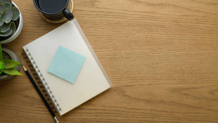 Top view of notebook, pencil, sticky note, coffee cup and copy space on wooden table, mock up sceneの写真素材