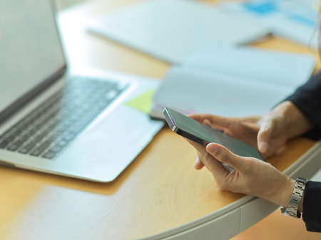 Side view of businessman using smartphone in his hands on workspace with laptop and supplies